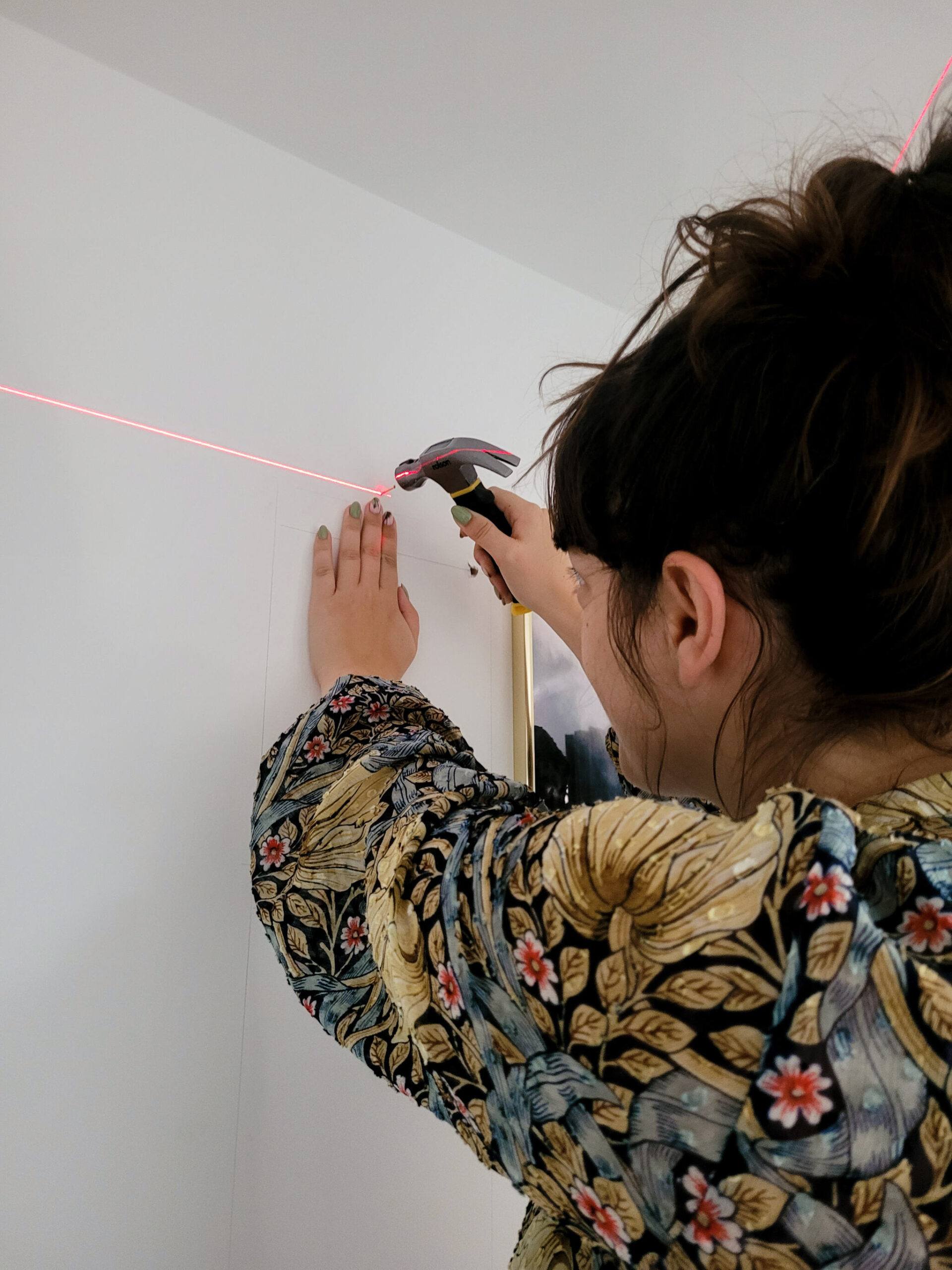Jessica hammers in a nail to hang her picture, assisted by a laser level
