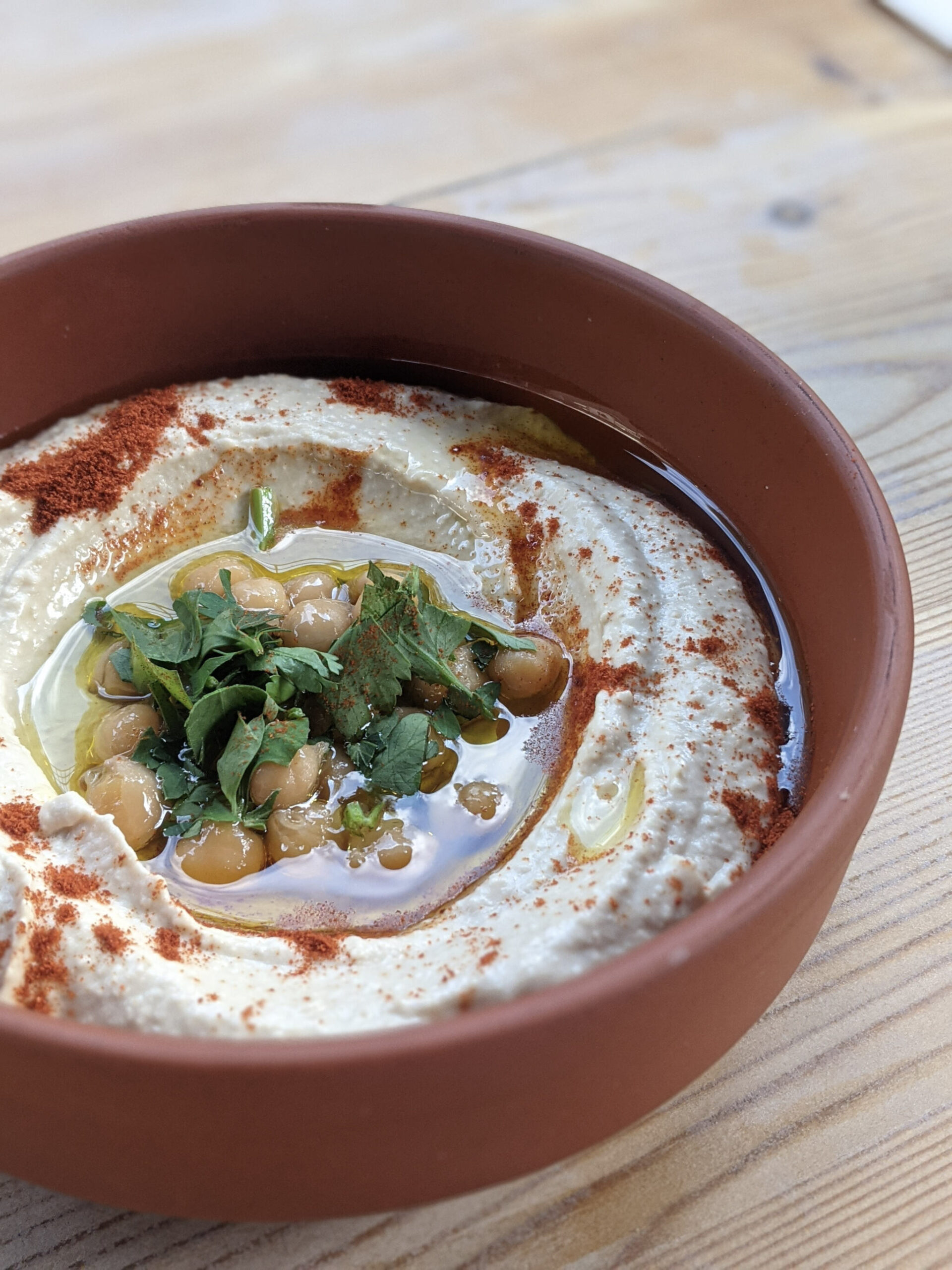 Hummus sits in a terracotta bowl, topped with chickpeas and paprika