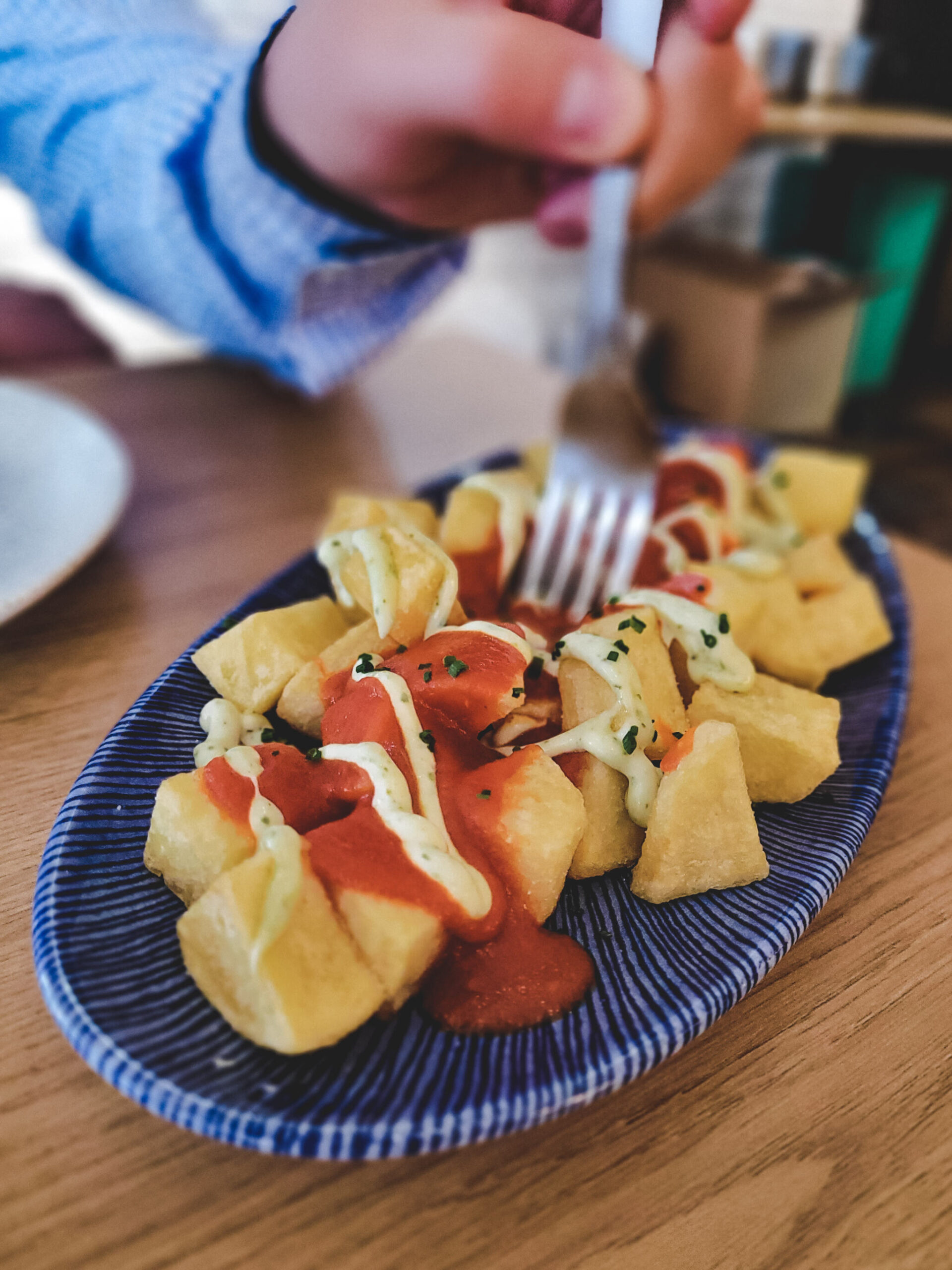 A hand digs a fork into a dish of patatas bravas at Ole Tapas
