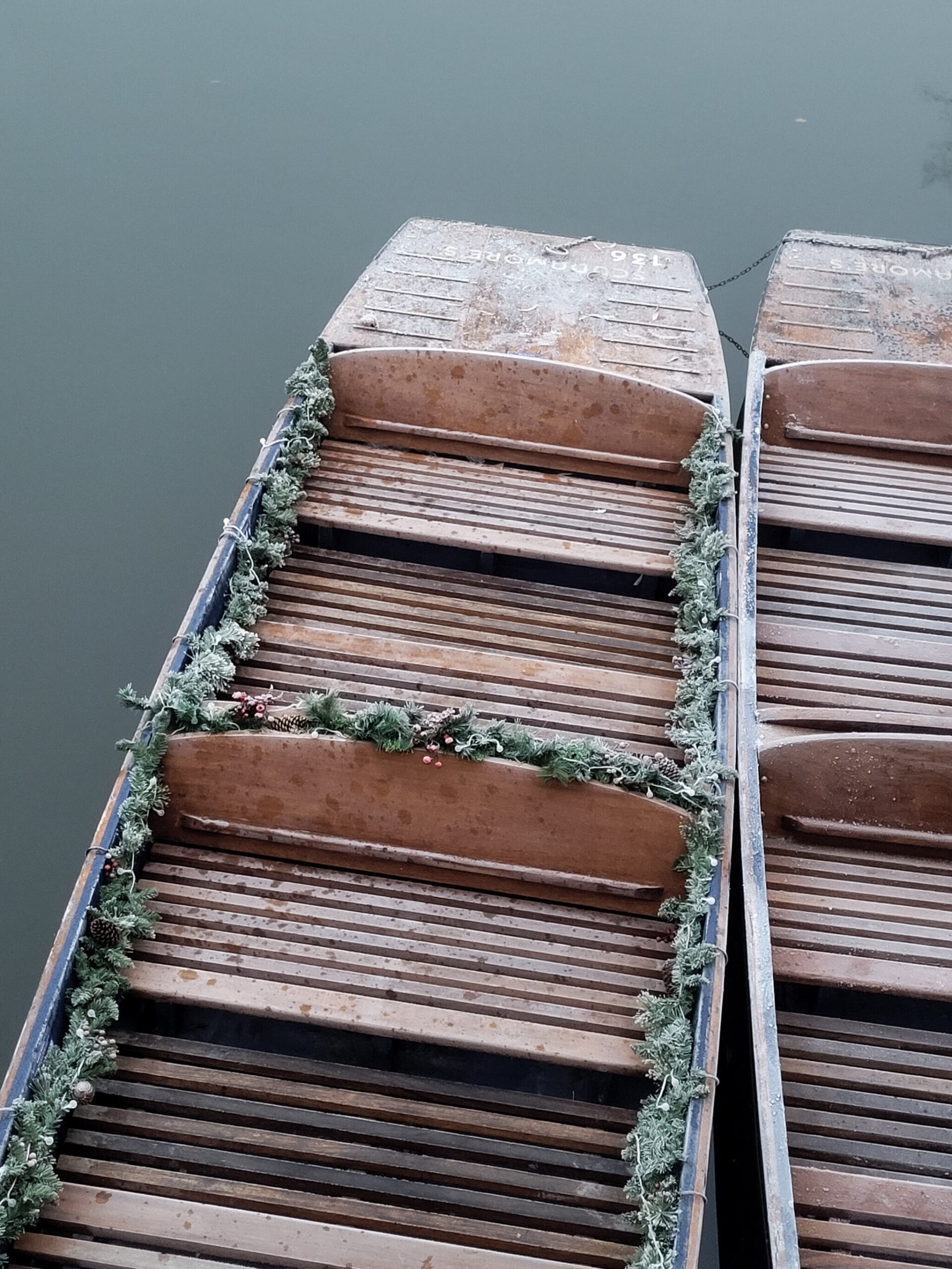 Two punts, edged with tinsel, sit unoccupied in the River Cam