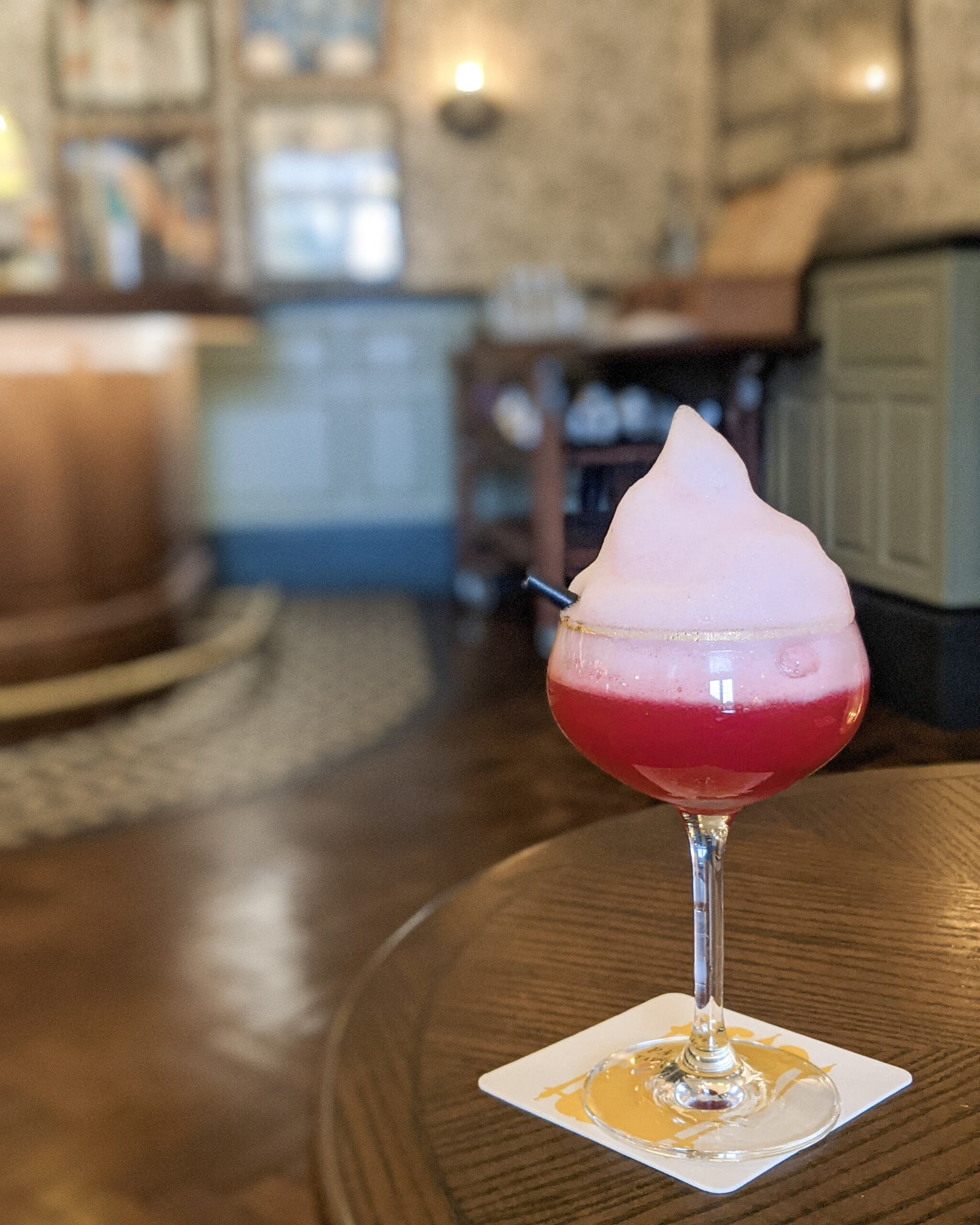 Bloomsbury Boozer, a red cocktail in a martini glass topped with a giant foam, sits on a table